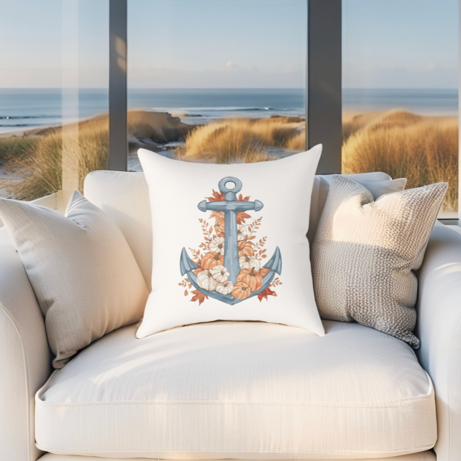 Decorative fall pillow with an anchor design and leaves on a white couch by a window with a beach view.