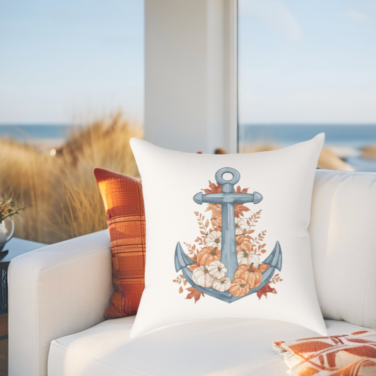 Decorative fall coastal pillow with an anchor, leaves, and pumpkin design on a couch by a window with a view of the ocean.