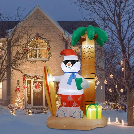 Inflatable snowman with palm tree and gift in front of a decorated house at night.