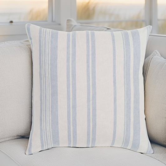 Coastal farmhouse pillow adding soft blue tones to a bright seaside living room.