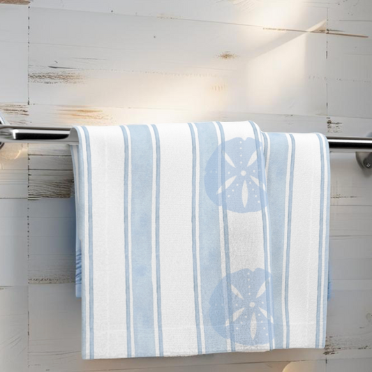Light blue coastal face towel with sand dollar design hanging on rack in beach-themed bathroom.