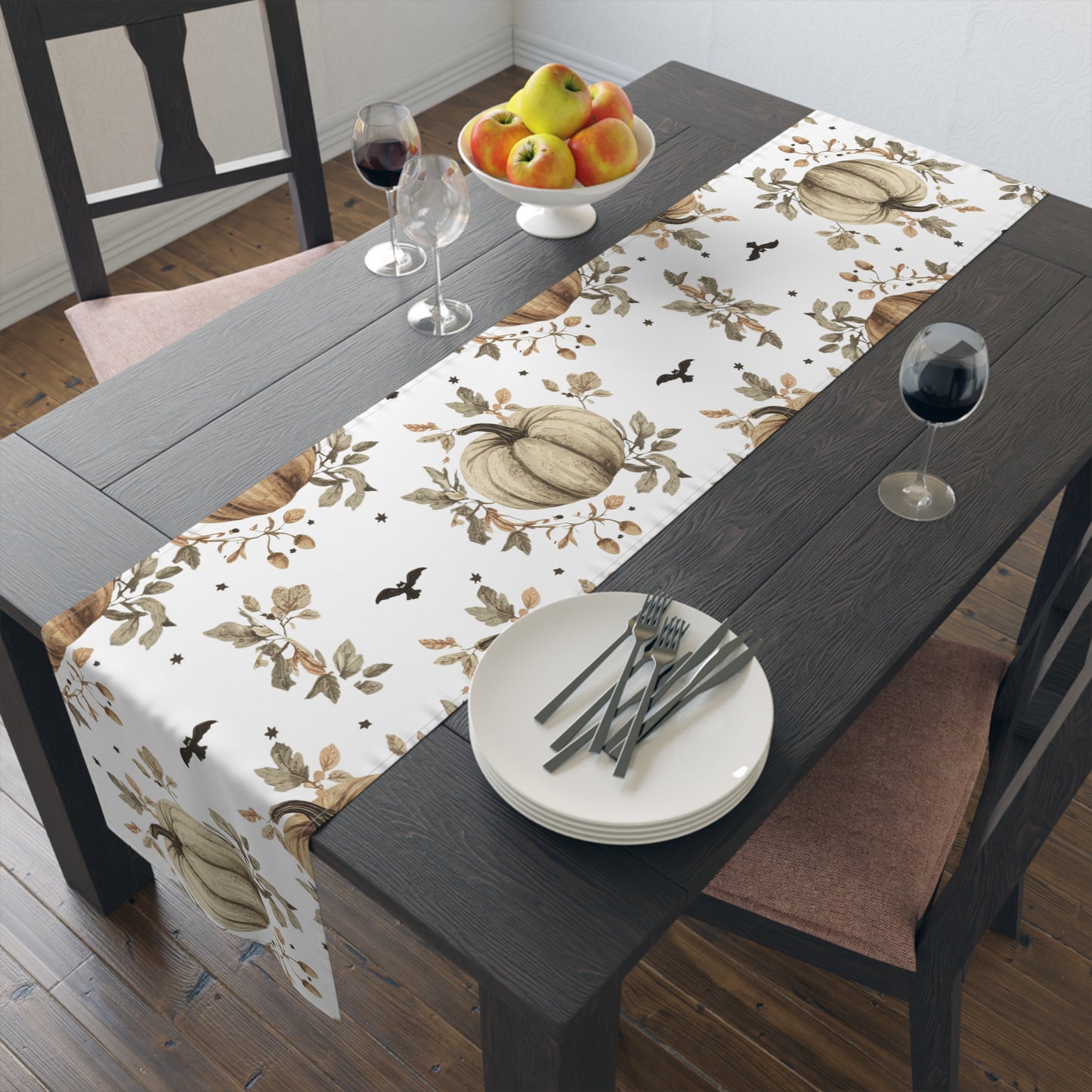 Dining table with a decorative tablecloth featuring pumpkins and leaves, set with plates, cutlery, and wine glasses.