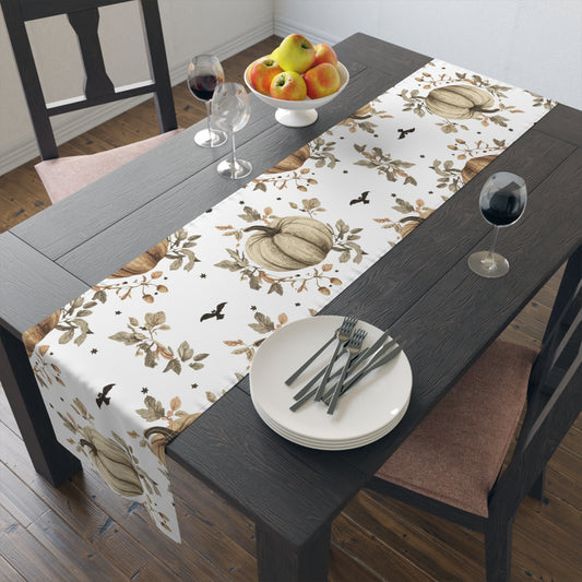 Dining table with a decorative tablecloth featuring pumpkins and leaves, set with plates, cutlery, and wine glasses.